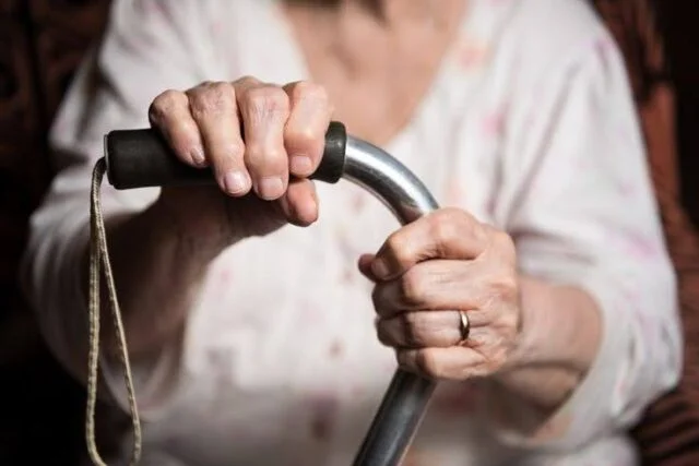 Elderly hands gripping a walking stick handle with both hands