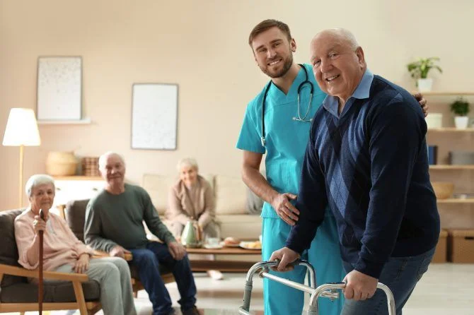 Caregiver helping elderly man use a walker in a care facility
